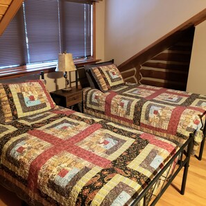 A bedroom with two beds, a nightstand, a lamp, and a window with blinds. - Two story authentic log construction home, built in 1936 with two fireplaces. (Custer)
