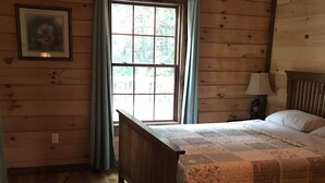 A wooden-paneled room with a bed, a window with curtains, and a framed picture on the wall.
