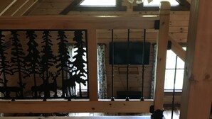 A wooden interior with a sloped ceiling, a ceiling fan, a window with a view, and a wall-mounted TV.