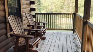 A wooden deck with Adirondack chairs and a view of a forest.