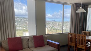A living room with a sofa, a small table, and a dining area with chairs. - Pacific Monarch Top Floor Condo with Ocean, City and Mountain Views! (Honolulu)