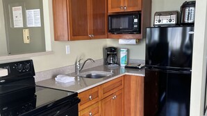 A kitchen with wooden cabinets, a black stove, a microwave, a toaster, and a refrigerator. - Pacific Monarch Top Floor Condo with Ocean, City and Mountain Views! (Honolulu)