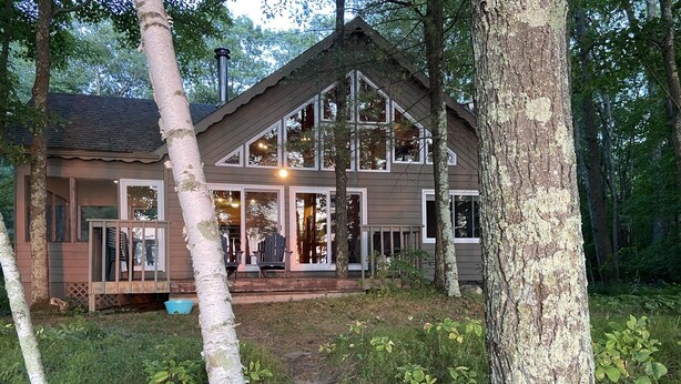 Mökki, jossa on suuri kuisti, useita ikkunoita ja savupiippu.