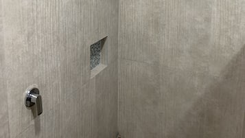 Ein Duschbereich mit vertikal befliester Wand, einer Duschbrause und einem kleinen Fliesenregal.