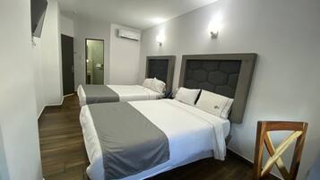 Ein Hotelzimmer mit zwei Betten, Holzboden, Klimaanlage und einem an der Wand montierten Fernseher.