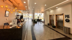 Een hotel lobby met een receptiebalie, een zithoek, liften en een groot raam met uitzicht op de straat.