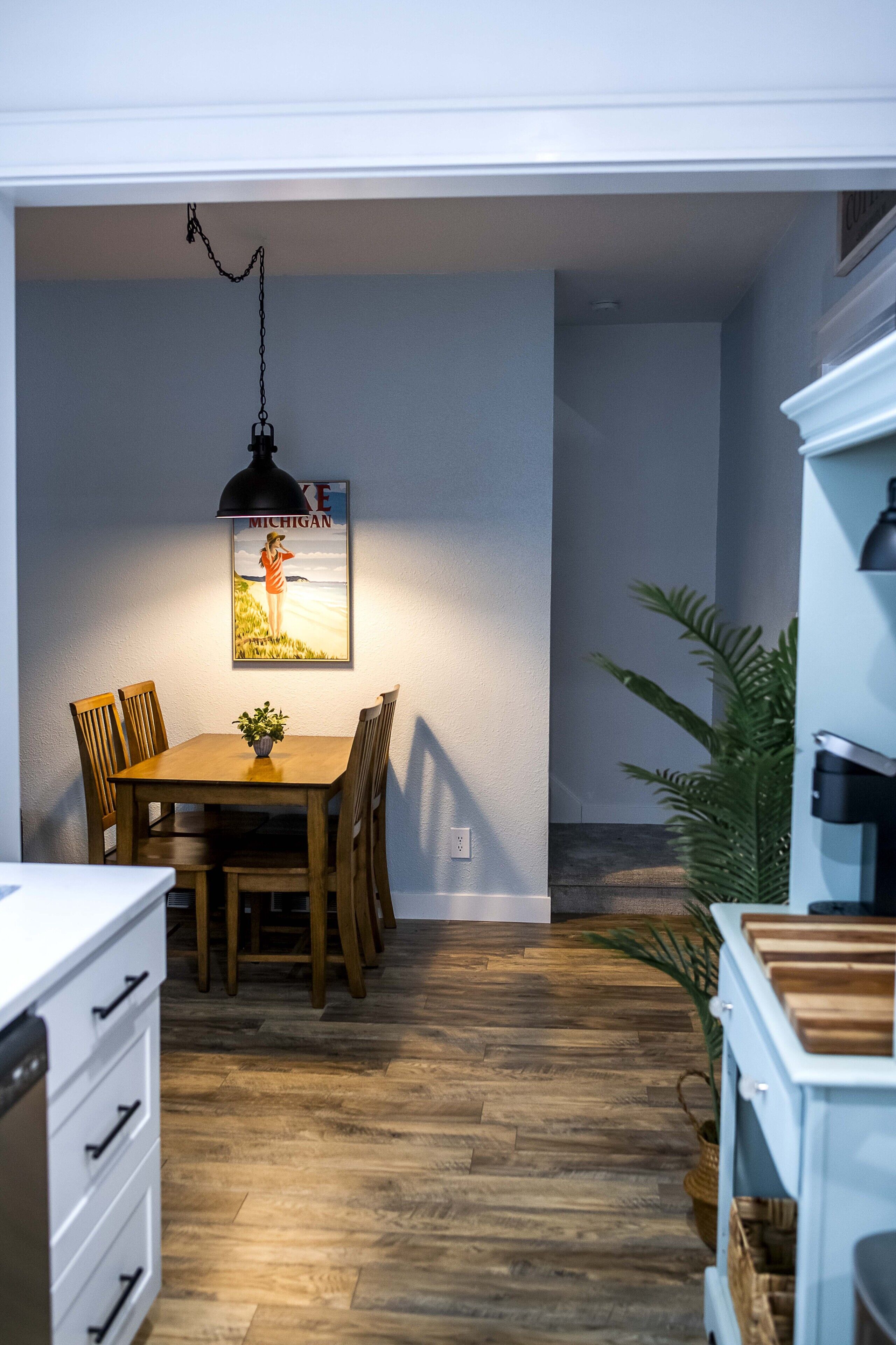 Un comedor con mesa y sillas de madera, una lámpara colgante y un cartel en la pared.