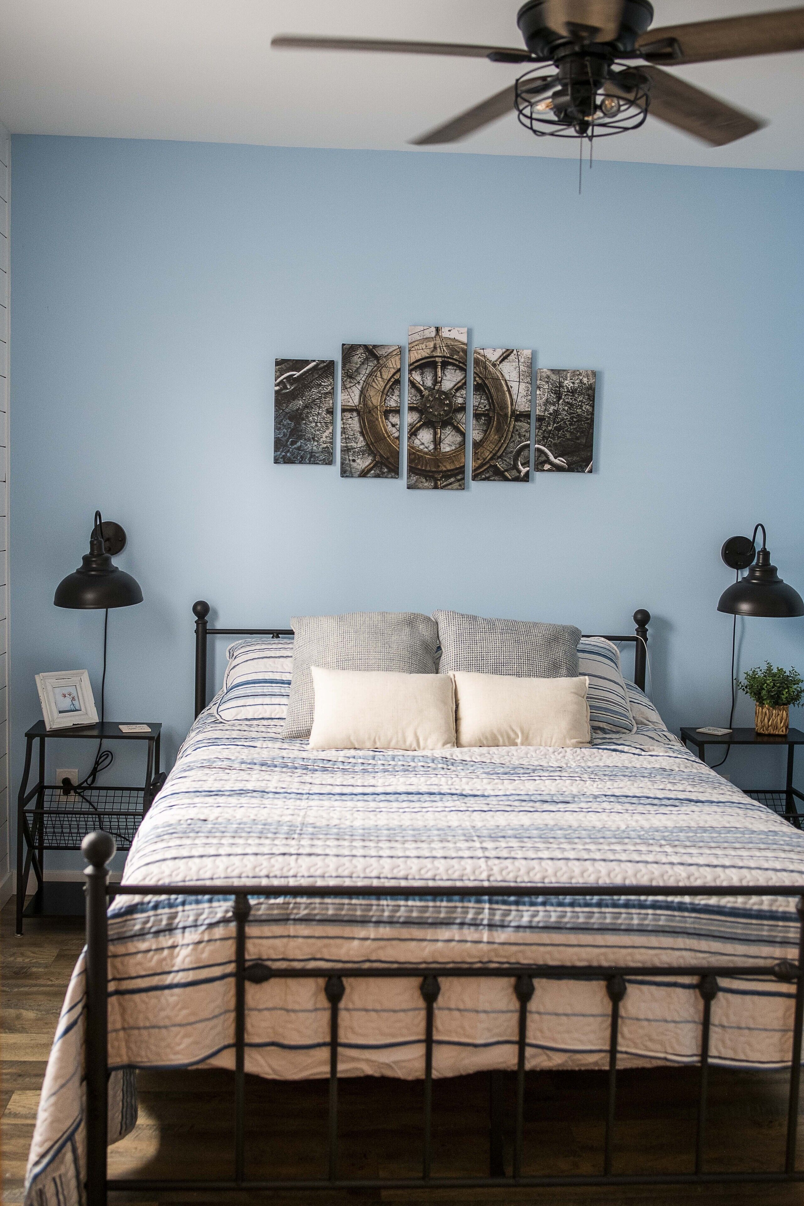 Un dormitorio con cama, ventilador de techo, obra de arte en la pared y lámparas de noche.