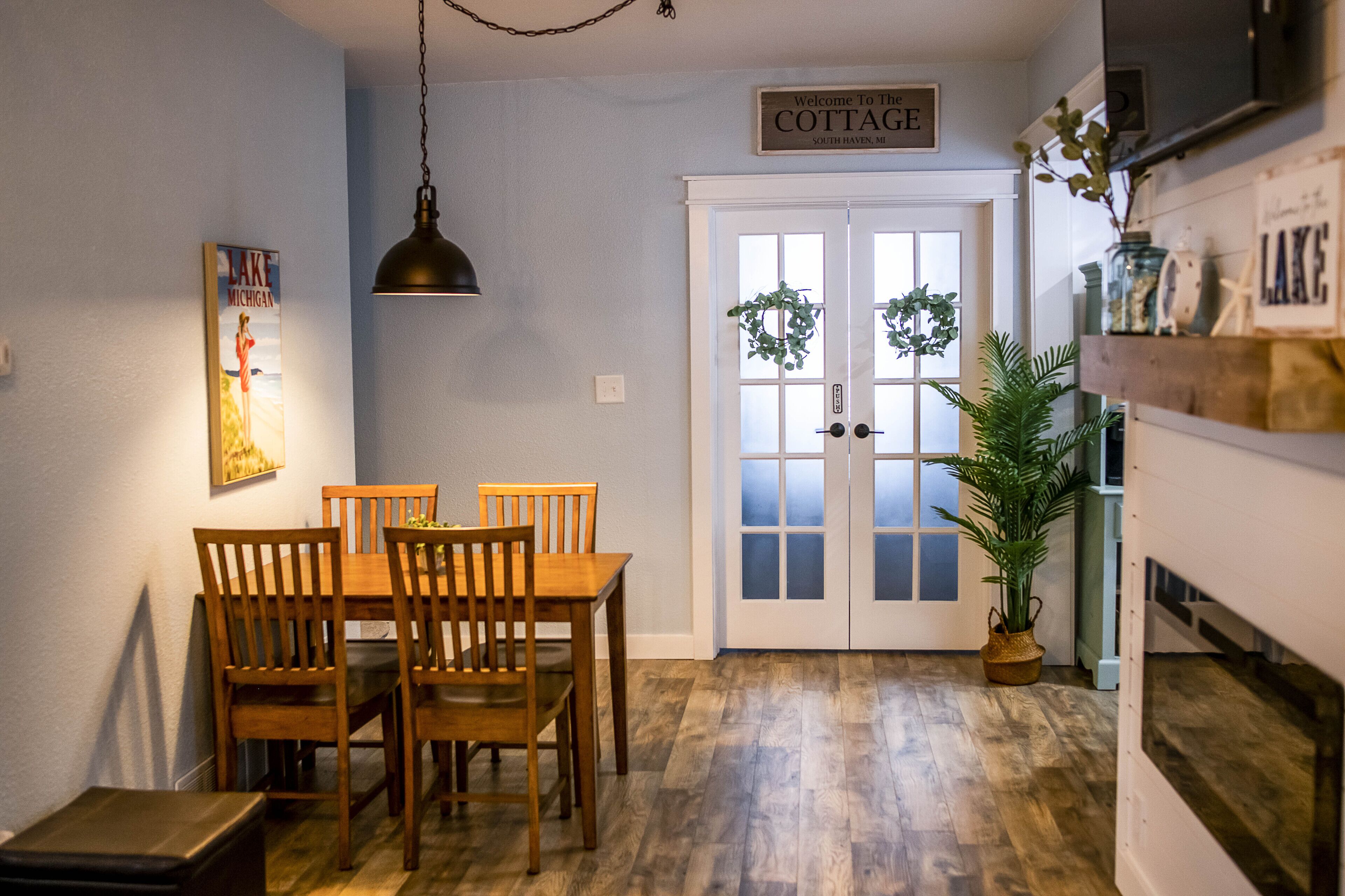 Ein Essbereich mit Holztisch und -stühlen, einer hängenden Pendelleuchte und einer Tür mit der Aufschrift "Welcome to the COTTAGE South Haven, MI".