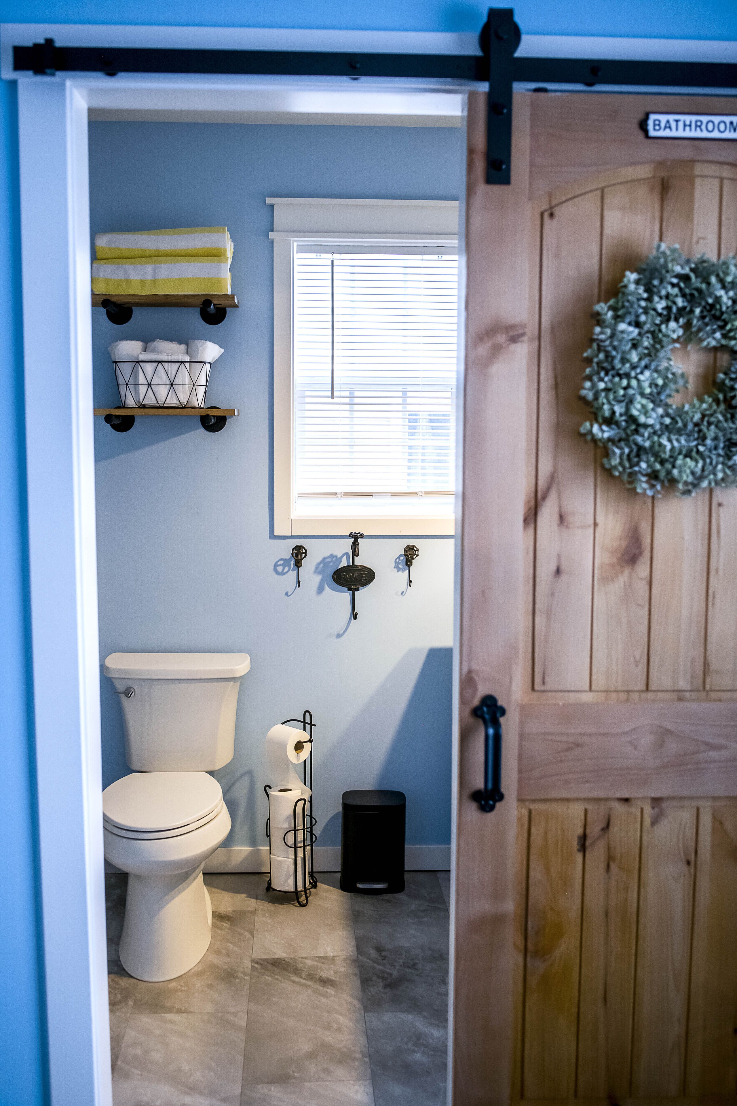 Un baño con inodoro, ventana, perchero para toallas y puerta de madera con adorno.
