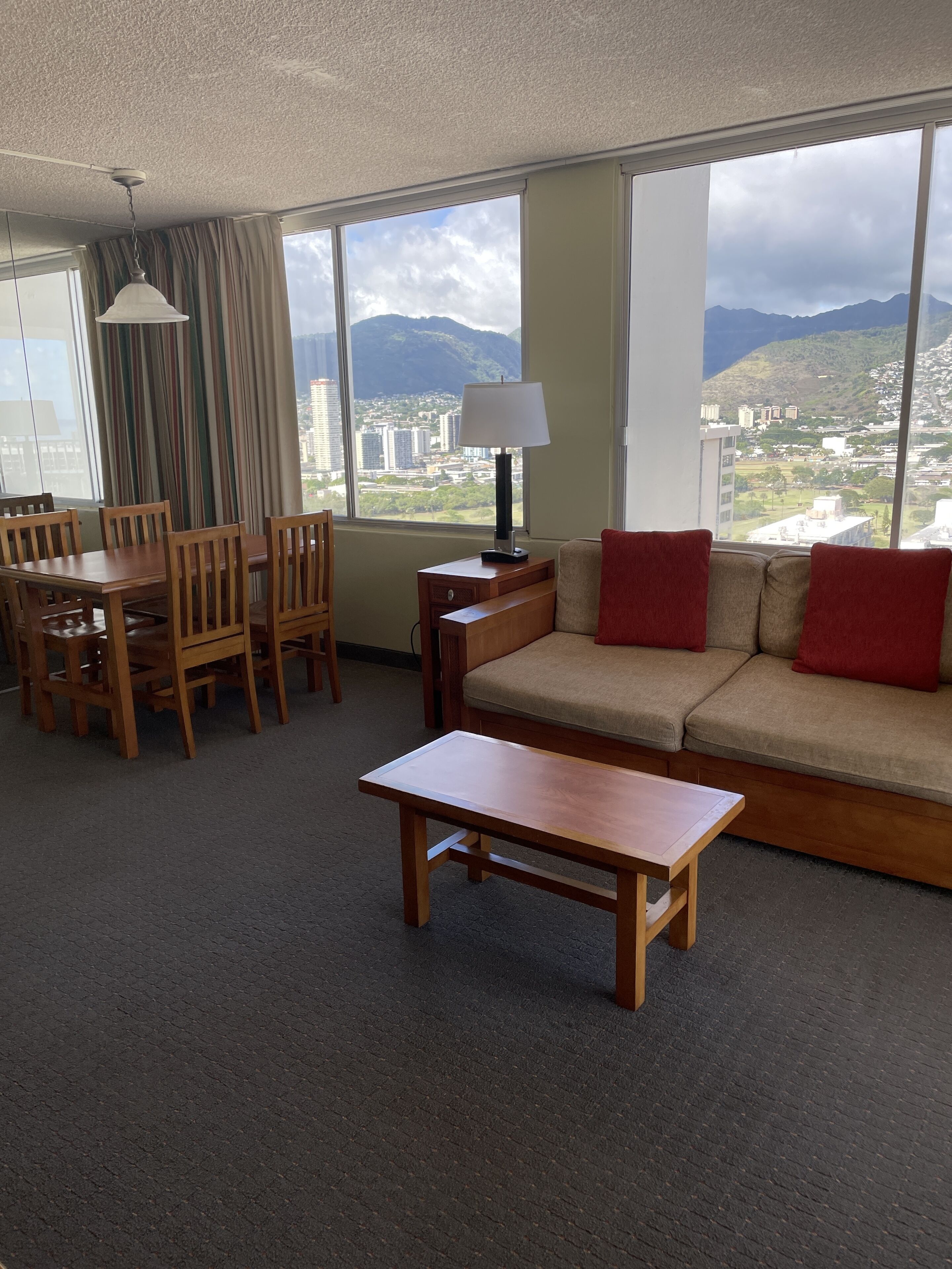 A hotel room with a dining area, a sofa, and a view of mountains and cityscape.