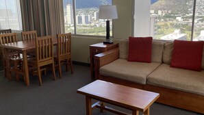 A hotel room with a dining area, a sofa, and a view of mountains and cityscape.