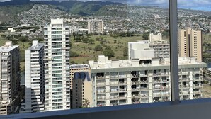 A high-rise building with multiple floors and balconies, overlooking a densely populated cityscape with various buildings and a mountain range in the background.