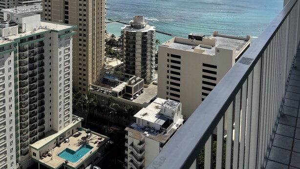 A high-rise building with a rooftop pool, surrounded by other buildings, overlooking a clear blue ocean.