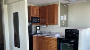 A compact kitchen with wooden cabinets, a black refrigerator, a microwave, a coffee maker, a sink, and an oven.