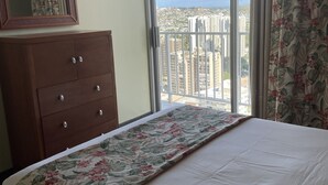 A hotel room with a bed, a dresser, and a large window offering a city view.