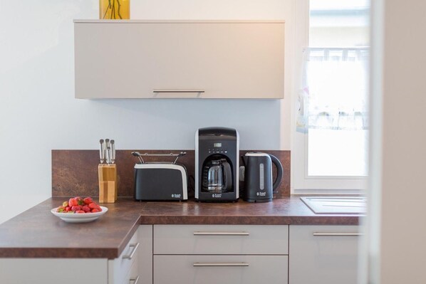 Una cocina moderna con tostadora, cafetera y hervidor en la encimera, y un plato de fresas.