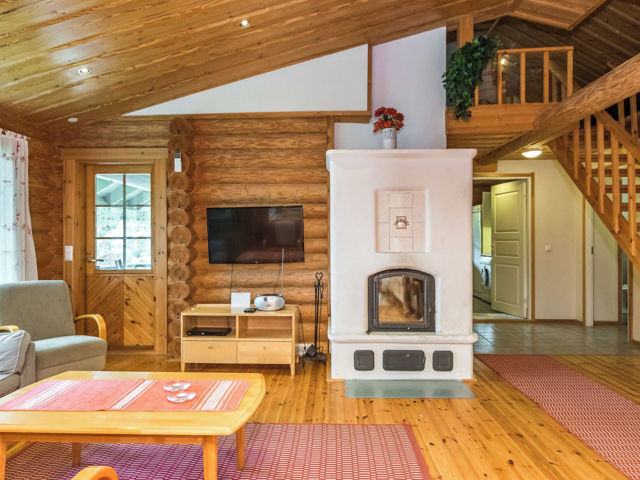 L’intérieur chaleureux d’un chalet, avec un revêtement mural en bois, une cheminée, un téléviseur et un escalier.