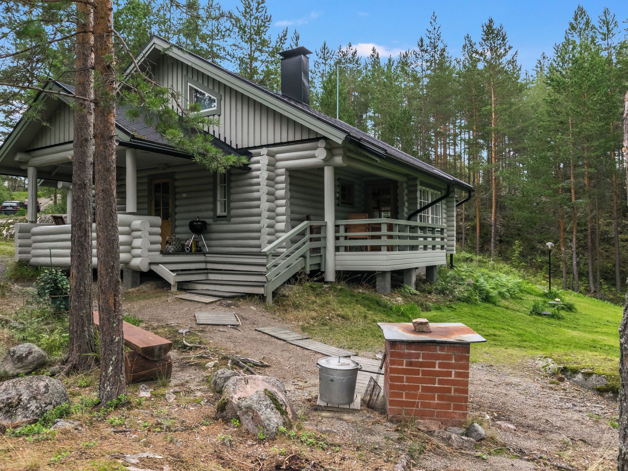 Une cabane en rondins avec un porche, une cheminée et une petite construction en briques.