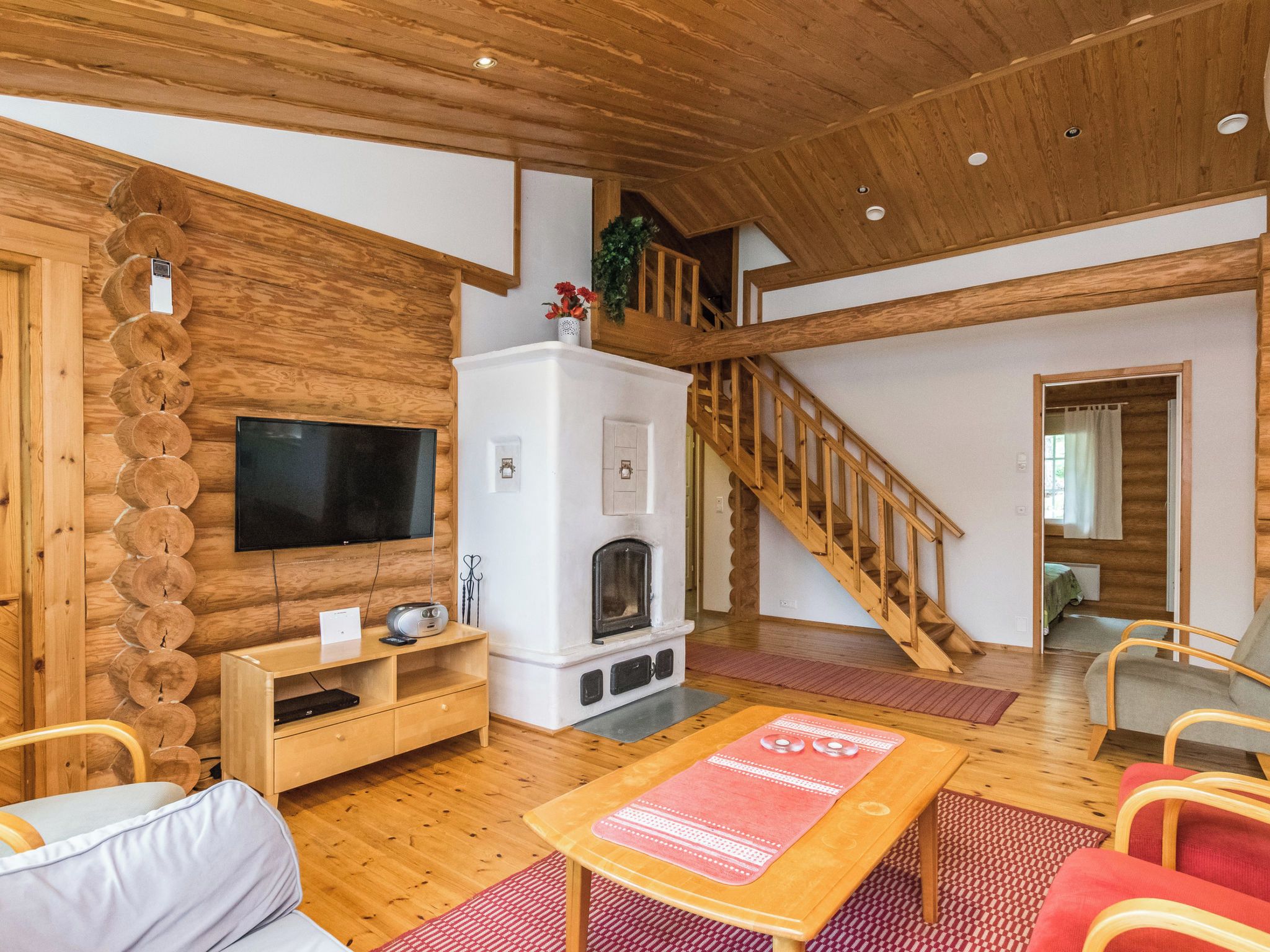 Un vaste salon doté d’un plafond en bois, d’une cheminée, d’un téléviseur et d’un escalier menant à un niveau supérieur.