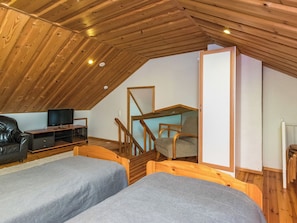 A loft bedroom with a sloped ceiling, wooden beams, a television, a sofa, a desk, and two beds. - Lahukka by Interhome (Puumala)