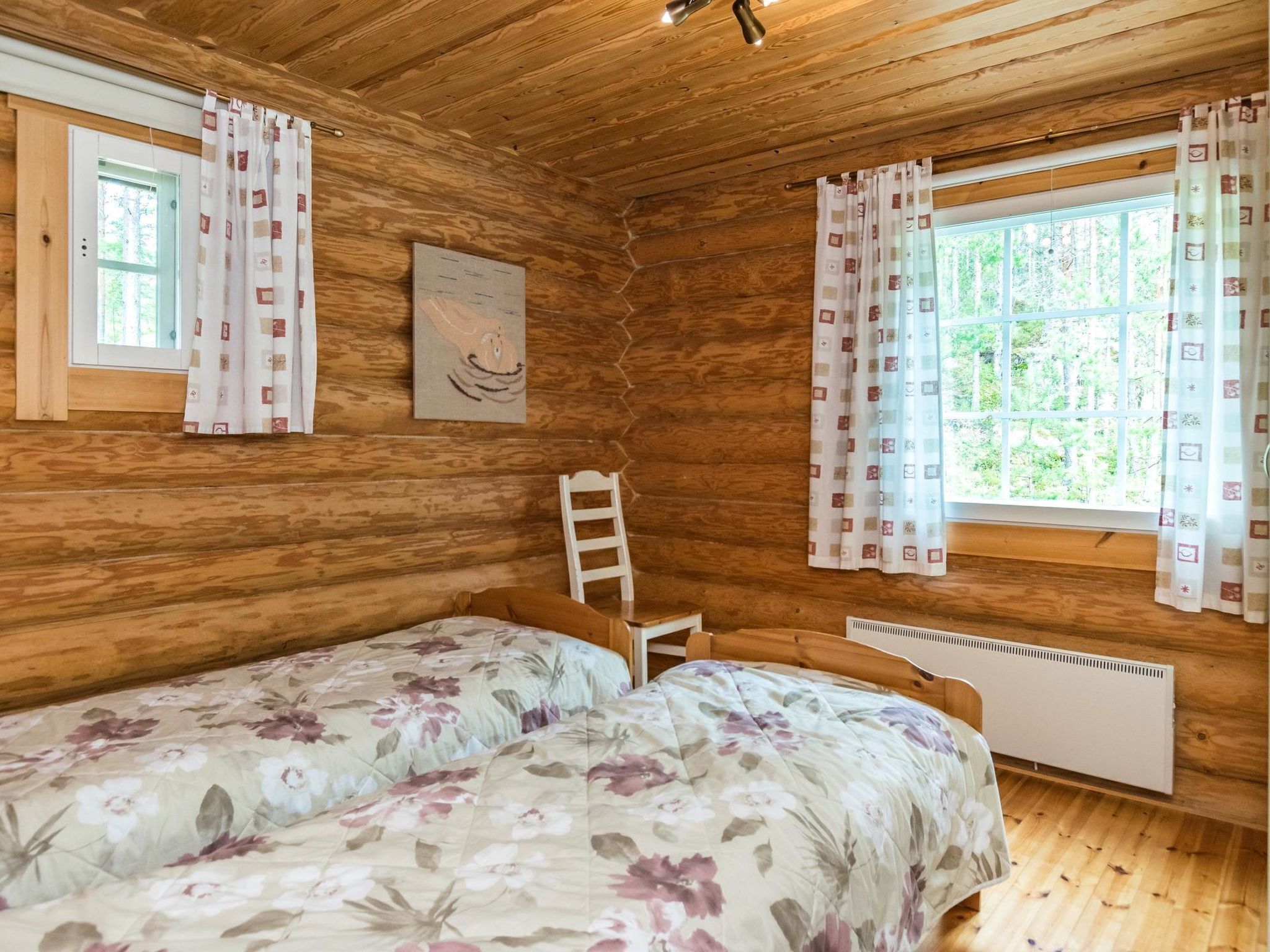 Una cabaña con dos camas, paredes de madera, una escalera, una ventana con cortinas y un radiador.
