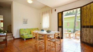 A dining area with a round table and chairs, a green sofa, and a window with curtains. - Wonderful  villa for 8 people with A/C, TV, terrace and pets allowed (Lignano Sabbiadoro)