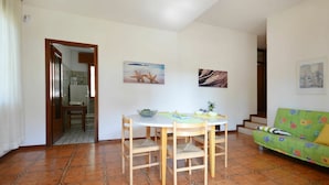 A dining area with a round table and chairs, a kitchen visible through an open door, and a green sofa with colorful cushions. - Wonderful  villa for 8 people with A/C, TV, terrace and pets allowed (Lignano Sabbiadoro)