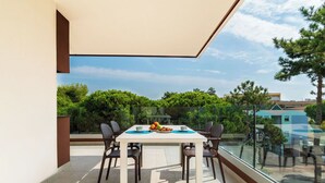 A modern dining area with a white table and four chairs, overlooking a scenic view of trees and buildings. - Nice apartment for 4 people with A/C, pool, WIFI, TV, terrace and pets allowed (San Michele Al Tagliamento)