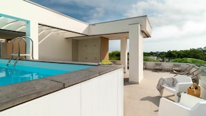A modern outdoor pool area with a clear blue pool, white lounge chairs, and a covered seating area. - Nice apartment for 4 people with A/C, pool, WIFI, TV, terrace and pets allowed (San Michele Al Tagliamento)