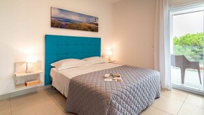 A bedroom with a large bed, two bedside tables with lamps, a painting on the wall, and a view through a window. - Nice apartment for 4 people with A/C, pool, WIFI, TV, terrace and pets allowed (San Michele Al Tagliamento)