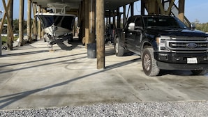 Un espace de stationnement couvert, doté d’un sol en béton, de piliers en bois et où est garé un camion noir, à l’abri.