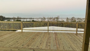 Une terrasse en bois avec une rambarde donnant sur une étendue d’eau et des arbres.
