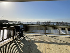 Una terraza de madera con una parrilla y vistas a un lago.