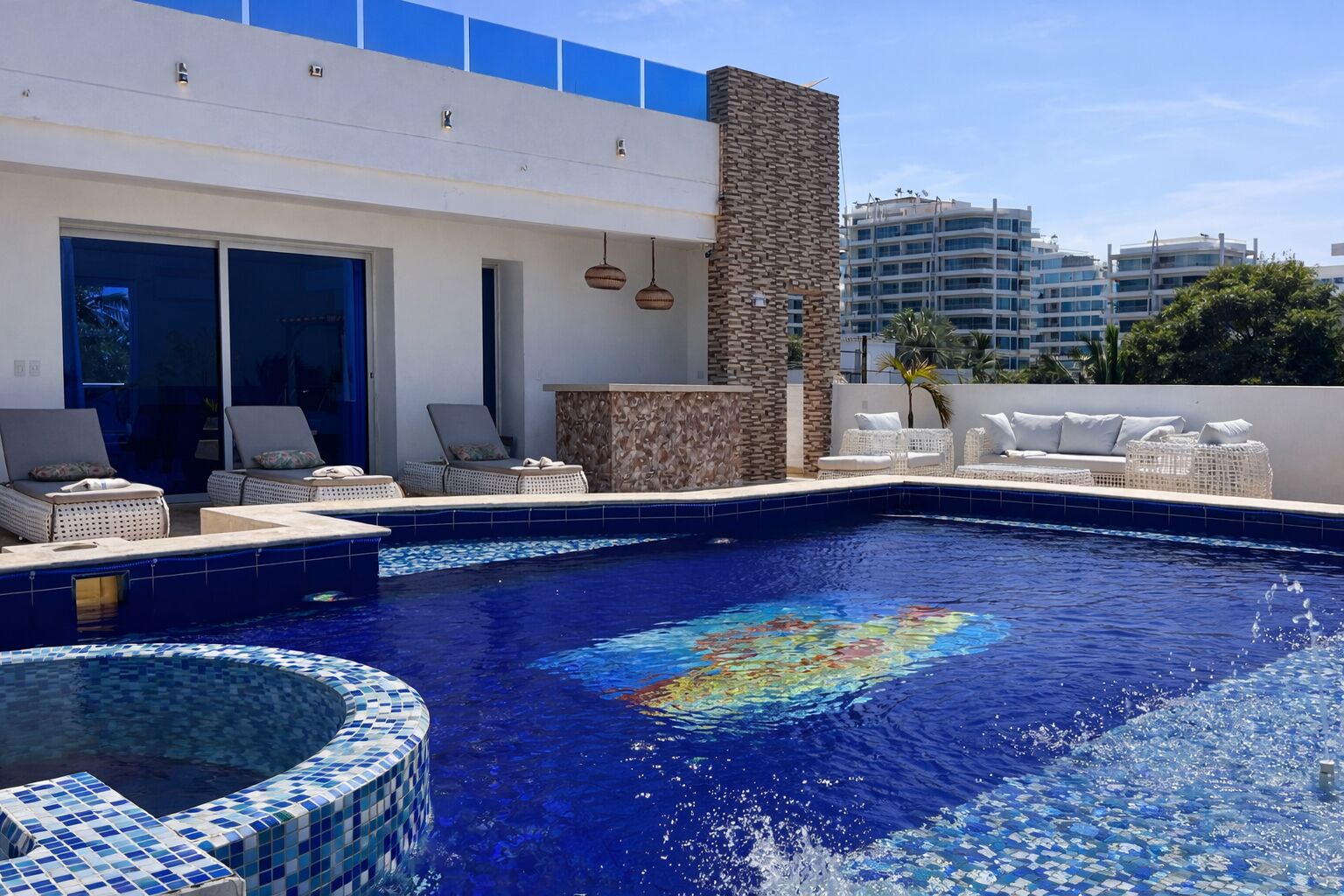 A swimming pool with lounge chairs and a hot tub, surrounded by a modern building with large windows and a stone wall.