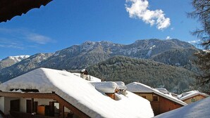 Ein Chalet mit schneebedecktem, geneigten Dach vor einer Kulisse aus schneebedeckten Bergen und blauem Himmel.