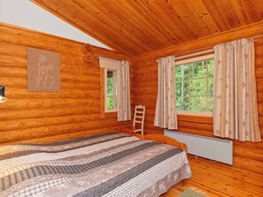Habitación de cabaña de madera con una cama, un ventanal con cortinas y un radiador.