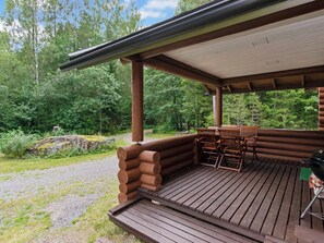 A covered wooden deck with a table and chairs, surrounded by a natural forest setting.