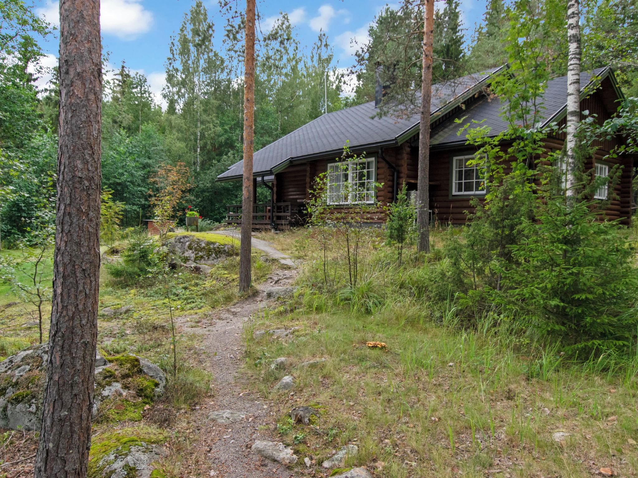 Eine Hütte, von Bäumen und Grün umgeben, mit einem Feldweg davor.