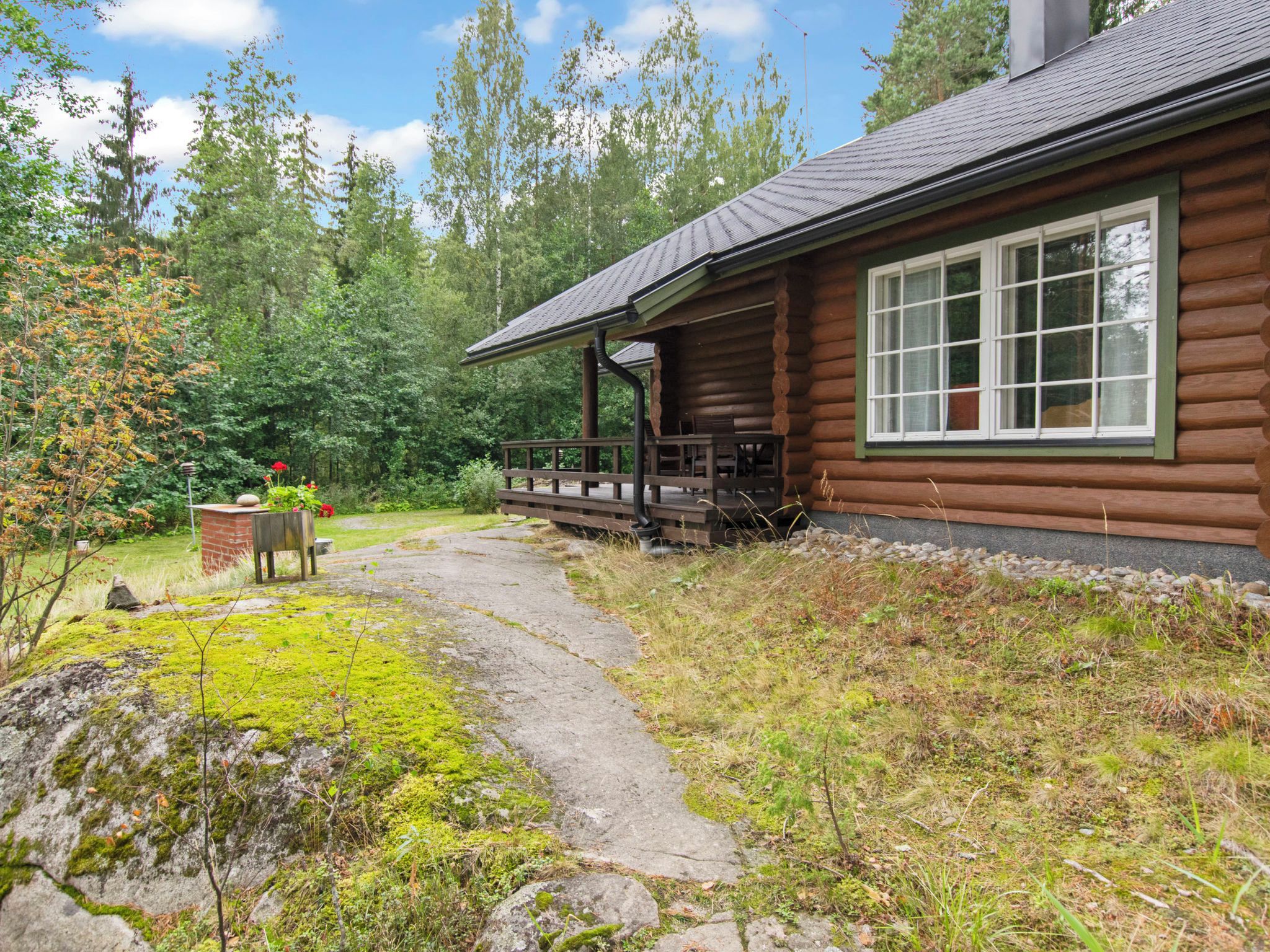 Eine Blockhütte mit Veranda, einem Steinweg und bewaldeter Umgebung.