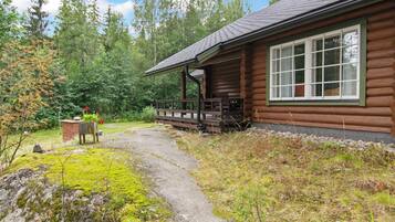 Eine Blockhütte mit Veranda, einem Steinweg und bewaldeter Umgebung.
