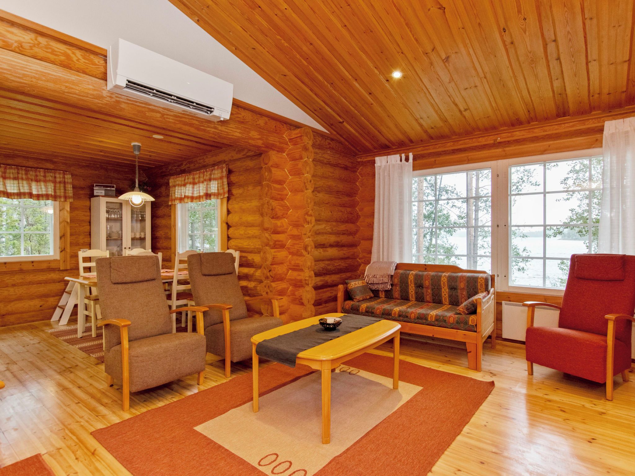 Ein rustikales Holzhaus-Interieur mit einer Couch, Sesseln, einem Esstisch und einem großen Fenster.