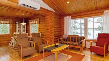 Ein rustikales Holzhaus-Interieur mit einer Couch, Sesseln, einem Esstisch und einem großen Fenster.