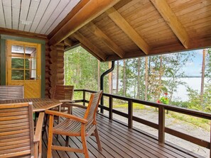 Una terraza de madera con una mesa y sillas, con vista a un lago y un bosque.