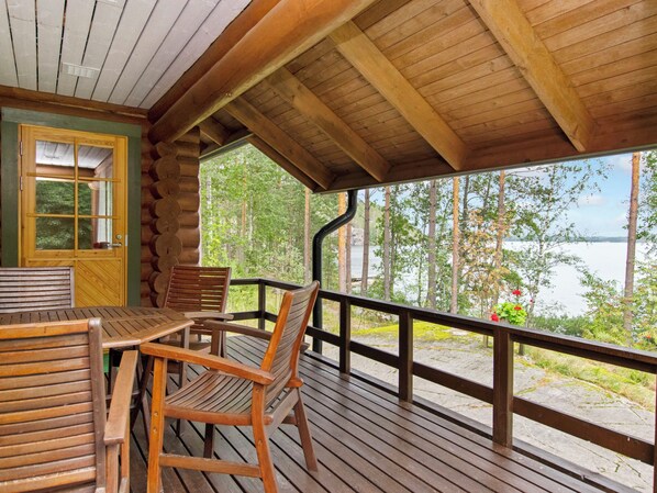 A wooden deck with a table and chairs, overlooking a lake and forest.