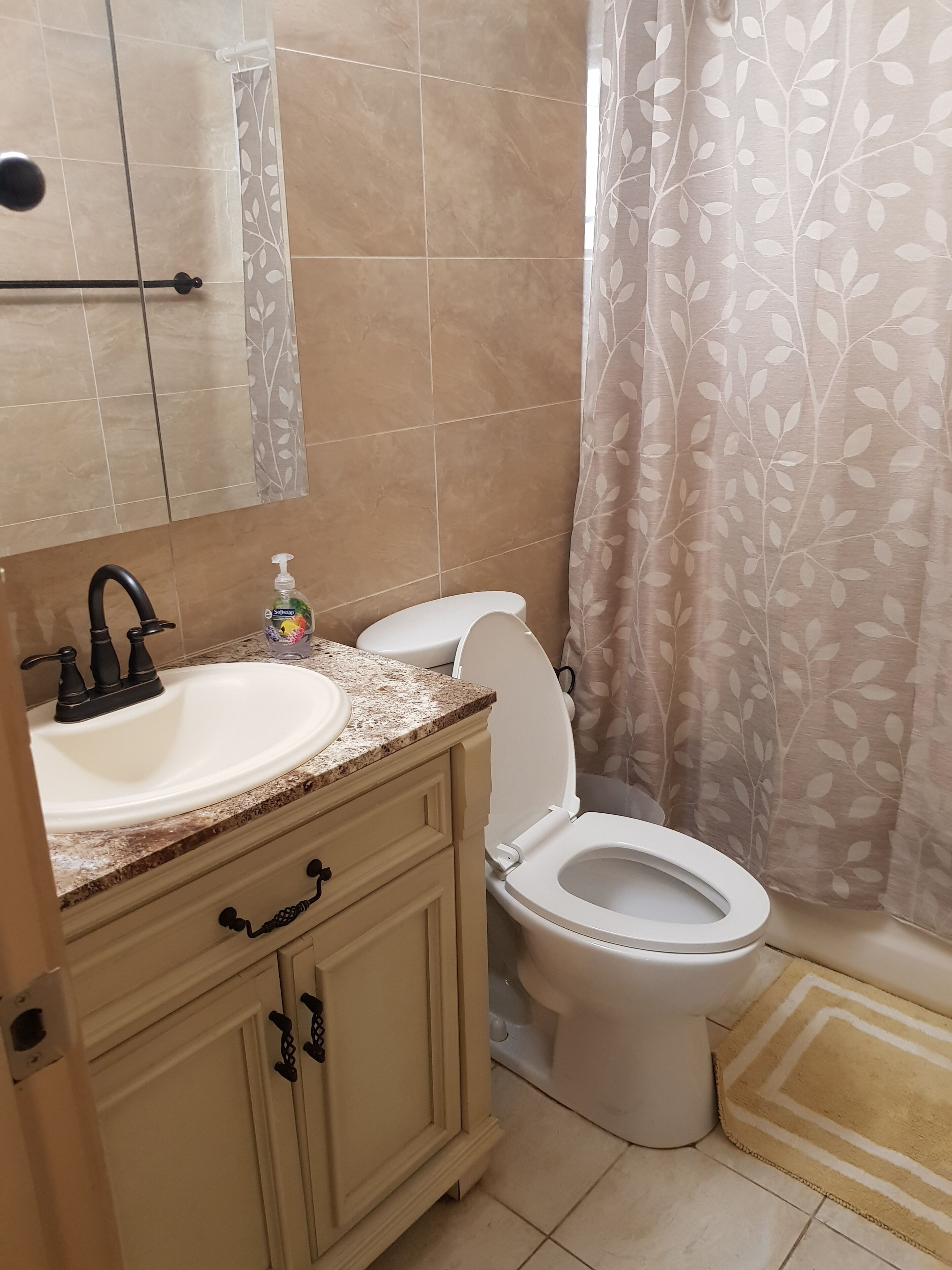 A bathroom with a sink, toilet, and a shower curtain with a leaf pattern.