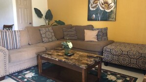 Sala de estar con un sofá, cojines estampados, una mesa de centro y un tapete floral.