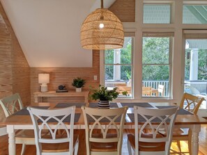 A dining area with a wooden table and chairs, a hanging light fixture, and large windows offering a view of the outdoors. - Large deck on main level and screened in porch, private crofter; access to both clubs! (Bald Head Island)
