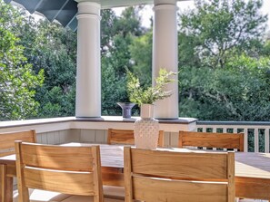 An outdoor patio with wooden chairs and a table, surrounded by white columns and greenery. - Large deck on main level and screened in porch, private crofter; access to both clubs! (Bald Head Island)