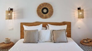 Ein Schlafzimmer mit einem Holzkopfende, zwei Nachttischen, einem gewebten Wandbild und zwei Wandleuchten.